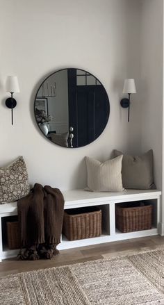 a white bench with baskets under a round mirror