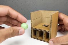 two hands are playing with an object made out of cardboard and green balls on the table