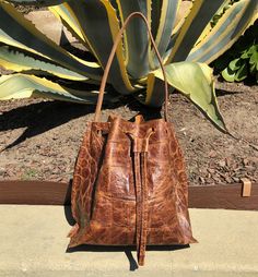 croco embossed cow leather color: bourbon brown lining: raw unlined dimensions: 9.5"h x 9.5"w x 6.5"d handle drop: 10" light weight One of a kind handmade in Los Feliz, CA Cognac Textured Leather Bucket Bag For Daily Use, Cognac Bucket Bag In Textured Leather, Cognac Textured Leather Bucket Bag, Brown Crocodile Pattern Travel Shoulder Bag, Brown Bucket Bag With Leather Handles For Errands, Brown Textured Leather Bucket Bag With Double Handle, Brown Bucket Bag With Leather Lining And Double Handle, Brown Textured Leather Bucket Bag For Shopping, Brown Leather Lined Bucket Bag With Double Handle