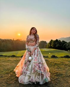 a woman standing on top of a lush green field next to a golf course at sunset