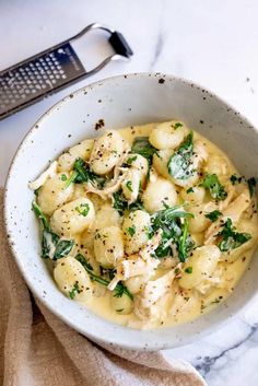 a white bowl filled with pasta and spinach on top of a marble countertop