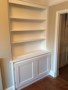 an empty room with white bookcases and wood floors