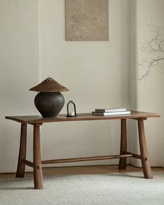 a wooden table with a vase and books on it in front of a white wall