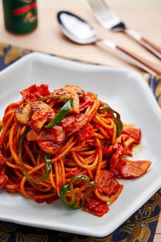 a white plate topped with pasta covered in sauce and peppers next to silverware on a wooden table