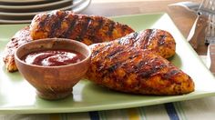 grilled chicken on a green plate with sauce in a small bowl next to it