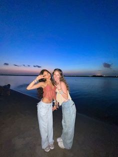 two women standing next to each other in front of the ocean at night with their arms around each other