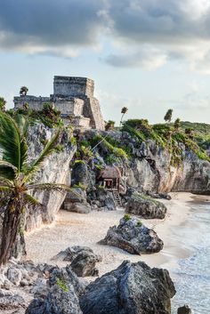 a beach with rocks and palm trees next to the ocean in front of a castle