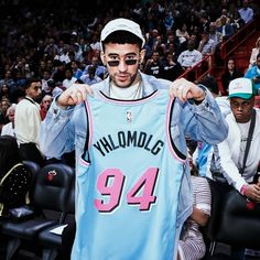 a man holding up a jersey in front of a crowd at a basketball game with other people watching