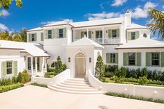 a large white house with green shutters on the front and stairs leading up to it