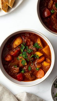 two bowls filled with stew and bread on top of a white countertop next to other dishes