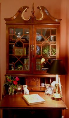 a wooden desk topped with a book and a glass case filled with books next to a lamp