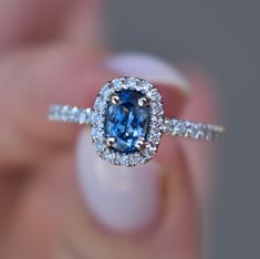 a close up of a person holding a ring with a blue and white diamond in it