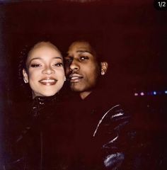 a man standing next to a woman in front of a dark background with lights on