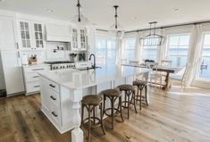 a large white kitchen with lots of counter space and stools in front of the island