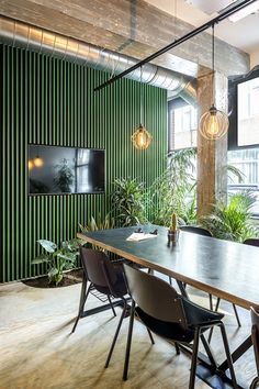 a long table with black chairs in front of a green wall and television mounted on the wall