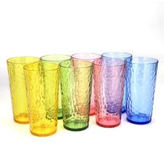 six different colored glass cups lined up in a row on a white surface, one is empty