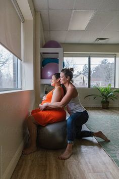 two women sitting on an exercise ball in the middle of a room with large windows