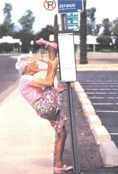 an older woman leaning up against a pole on the side of a road with her feet in the air