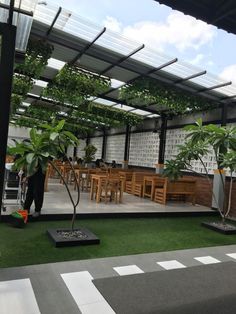 an outdoor dining area with green plants and wooden benches on the grass, under a pergolated roof