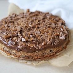 there is a cake with chocolate frosting and nuts on the top, sitting on some parchment paper