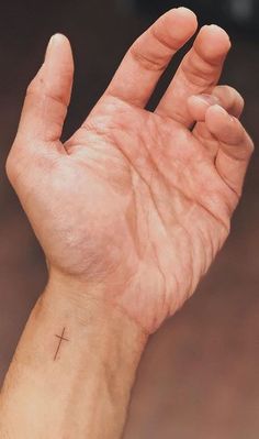 a person's hand with a cross tattoo on the middle of their left wrist