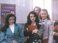 three women standing next to each other in front of desks with books on them