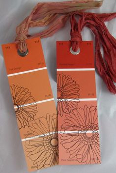 two tags with flowers on them sitting next to some string and yarn, one is orange and the other is pink