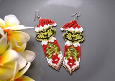 the grin face beaded earrings are on display next to some white and red flowers