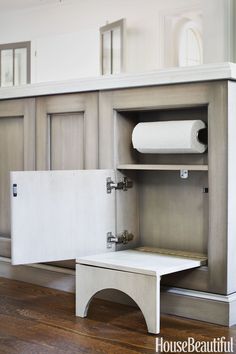 an open cabinet with toilet paper on the bottom and under it, in front of a wooden floor