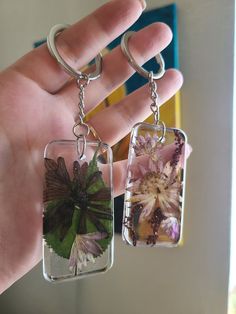 a hand holding two glass keychains with flowers on them and one has a flower in it