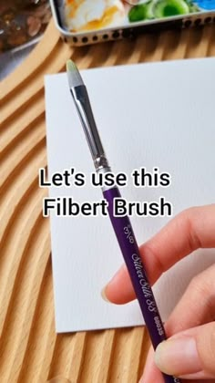 a person is holding a pen and writing on paper with the words, let's use this filbert brush