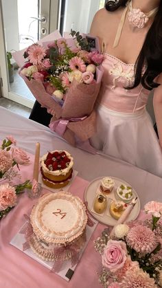 a woman in a pink dress holding a bouquet of flowers next to a table with cakes and cupcakes