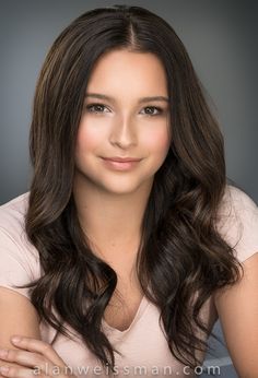 a woman with long hair posing for a studio photo in front of a gray background