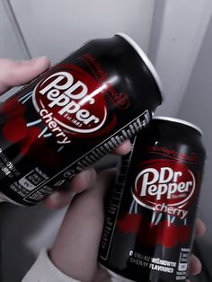 two cans of dr pepper are being held by someone