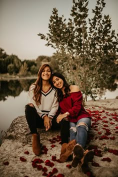 two women sitting next to each other in front of a lake with rose petals on the ground