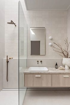 a white bathroom with two sinks and a shower stall in the corner, along with a large mirror on the wall