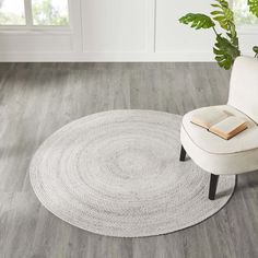 a white chair sitting on top of a wooden floor next to a book and potted plant