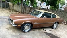 a brown car parked in a driveway next to a wooden fence