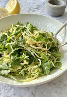 a white bowl filled with pasta and spinach on top of a marble countertop