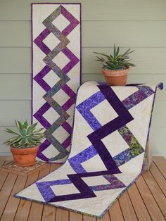 two quilts sitting next to each other on top of a wooden floor near a potted plant