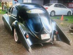 an old black car is parked in the dirt