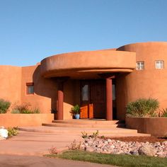 an adobe - style house in the desert with grass and rocks on the front lawn