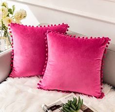 two pink pillows sitting on top of a white fur covered bed next to a plant