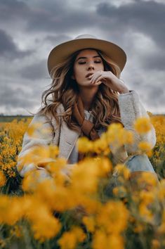 a woman wearing a hat sitting in a field of flowers with her hands on her face