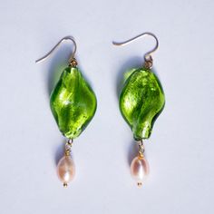 two green earrings with pearls hanging from them on a white surface, one in the shape of a leaf