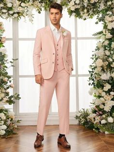 a man wearing a pink suit and shoes standing in front of a floral arch with white flowers