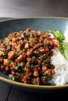 a blue bowl filled with rice and meat on top of a wooden table next to a green leafy garnish