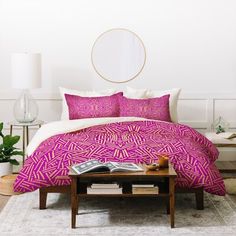 a bed with pink and red comforter in a white room next to a coffee table