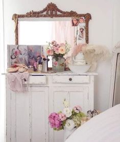 a white dresser with flowers and pictures on it's top, in front of a mirror