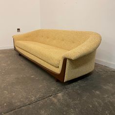 a yellow couch sitting on top of a cement floor next to a white wall in an empty room